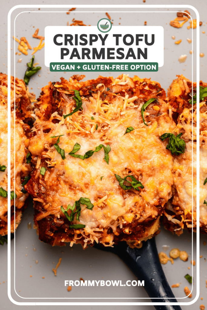 Baked tofu parmesan topped with vegan cheese and marinara sauce on baking sheet