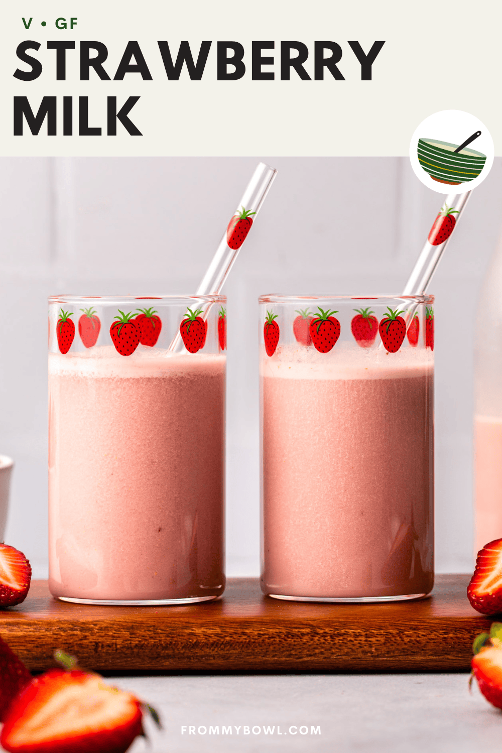 two glasses of vegan strawberry milk served on a cutting board with half-cut strawberries as decoration
